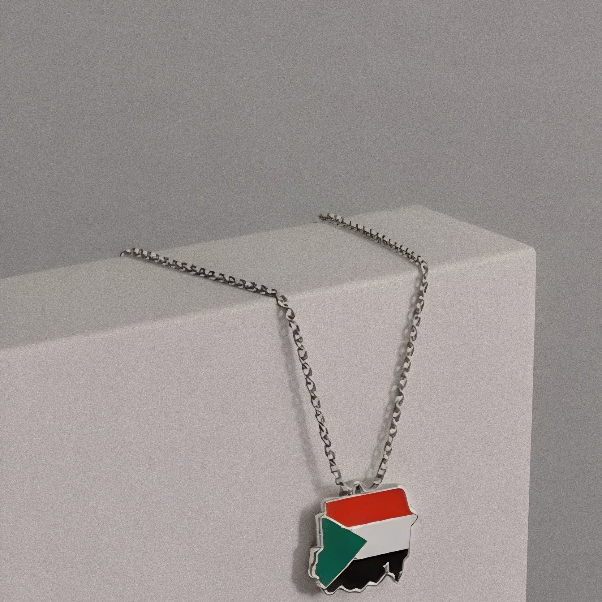 Necklace with a flag pendant on a gray background, featuring Balance Studios branding.
