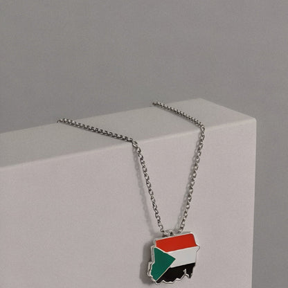 Necklace with a flag pendant on a gray background, featuring Balance Studios branding.